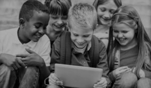 Cinco niños mirando la pantalla de una tablet sonrientes